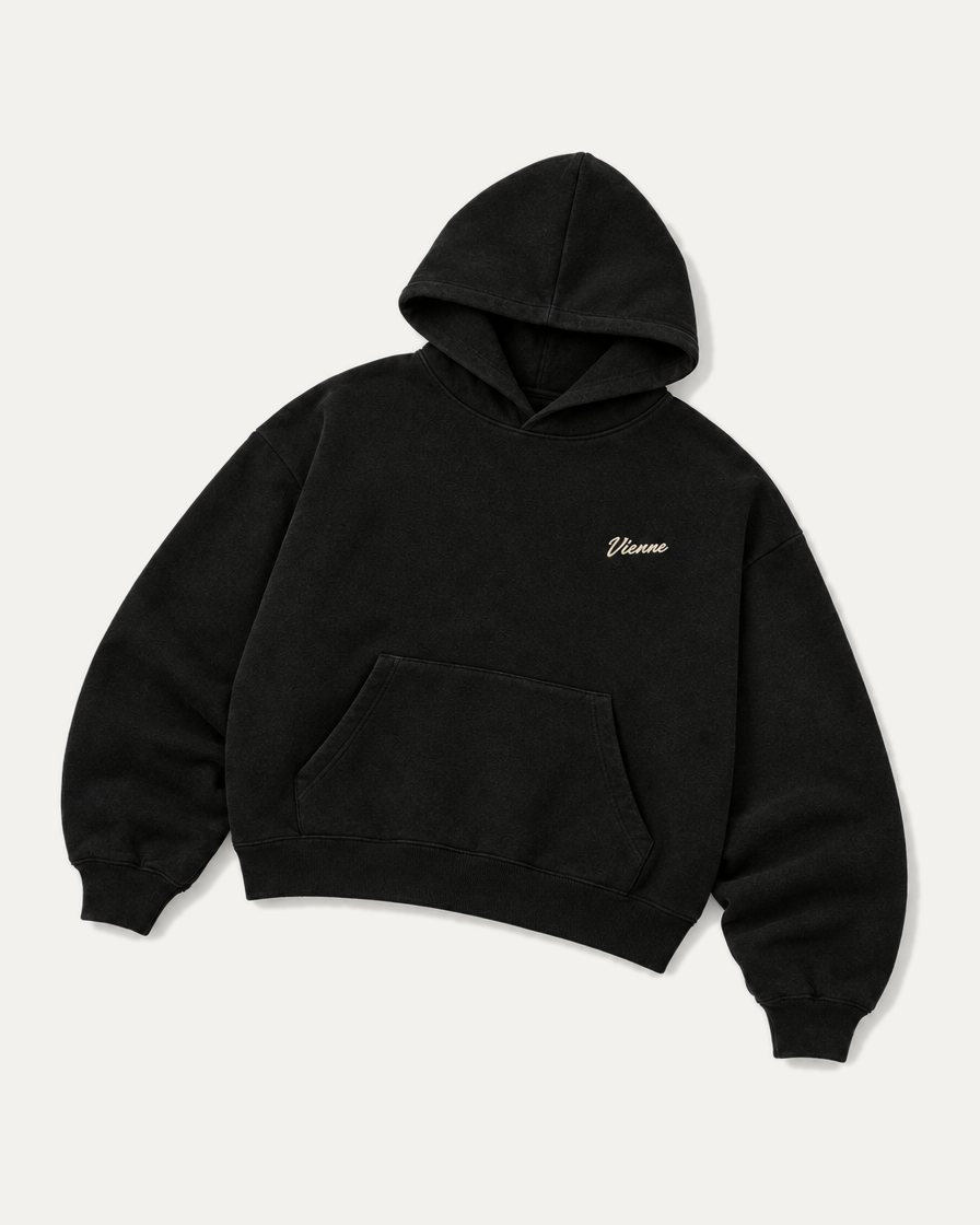 Concept image: black Signé Hoodie laid flat, cream Vienne script on the chest