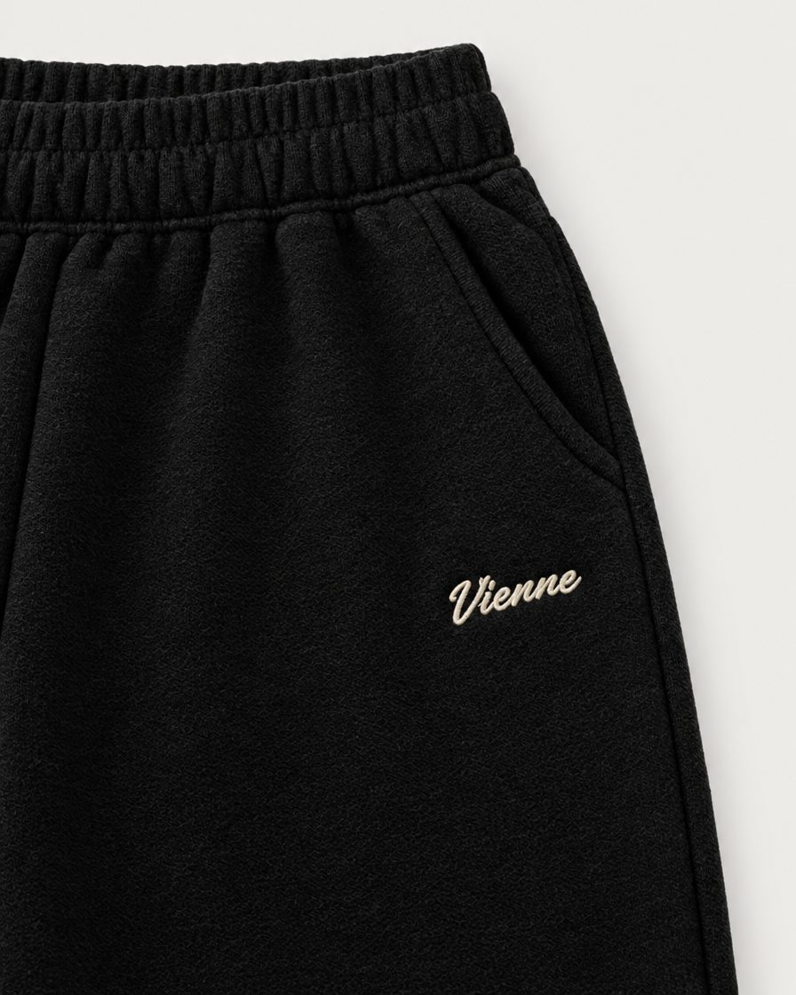 Concept image: close up of the elastic waist, slant pocket and cream Vienne script on the black Signé Sweatpant
