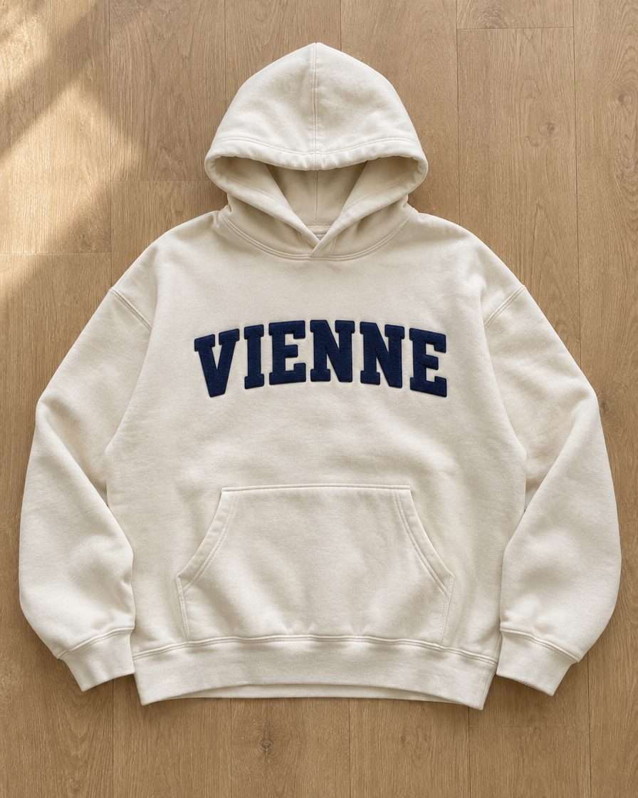 Concept render: cream hoodie with VIENNE in navy chenille letters across the chest