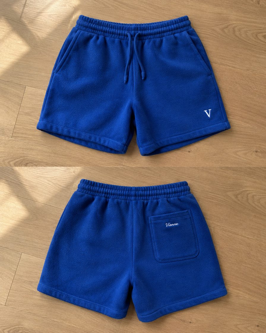 Concept render: cobalt fleece shorts, front with a white V monogram and back with a small script