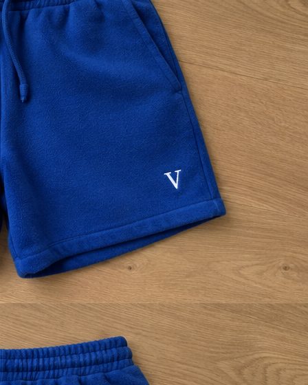 Concept render: cobalt fleece shorts, front with a white V monogram and back with a small script, close up of the detail