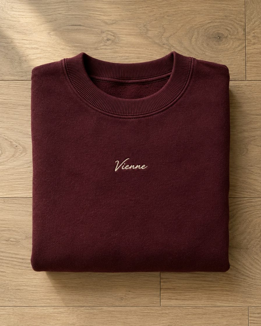Concept render: folded burgundy crewneck with a small cream Vienne script