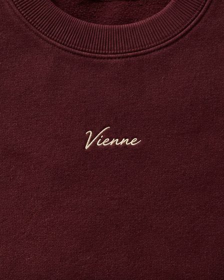 Concept render: folded burgundy crewneck with a small cream Vienne script, close up of the detail